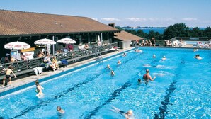 Ein Schwimmbecken mit mehreren Bahnen, Zuschauern und Sonnenschirmen.