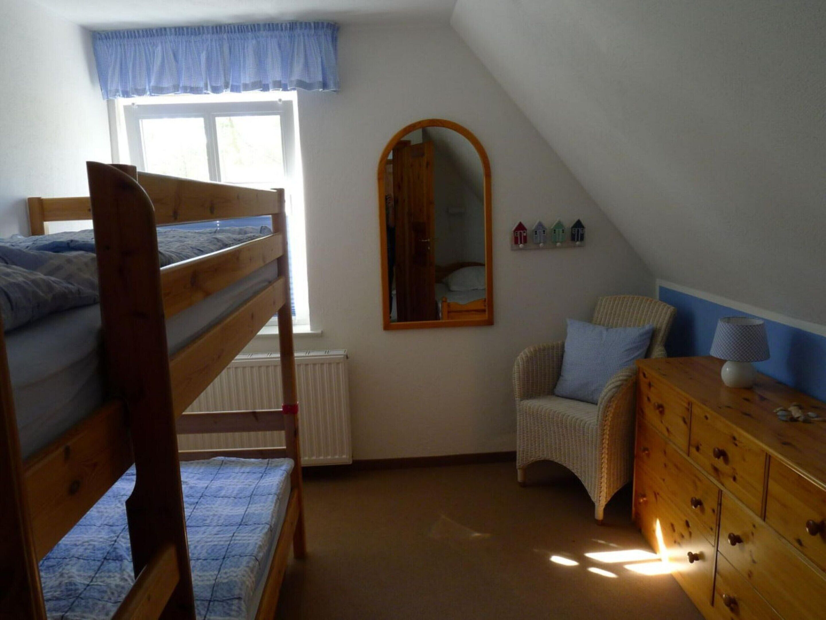 Ein Schlafsaalzimmer mit Etagenbetten, einem Schminktisch, einem Stuhl, einem Spiegel und einem Fenster mit Vorhang.