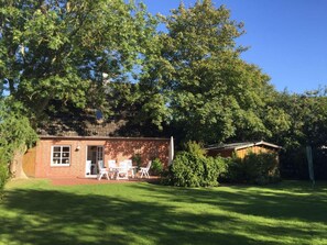 A small brick building with a patio area, surrounded by lush greenery and trees.