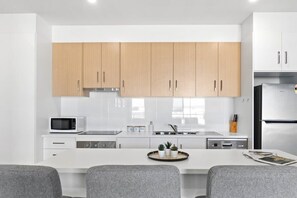Een moderne keuken met witte kasten, een magnetron, een fornuis en een koelkast.
