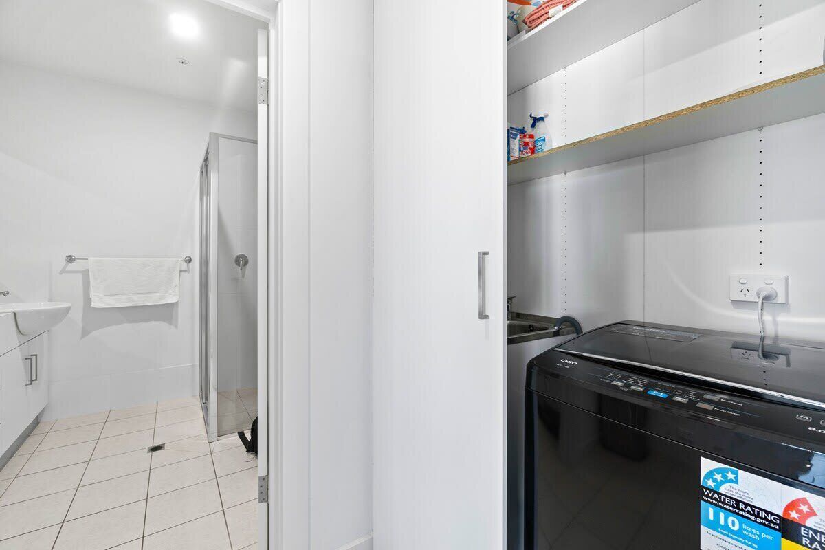 A bathroom with a white sink, a glass shower enclosure, and a black washing machine.