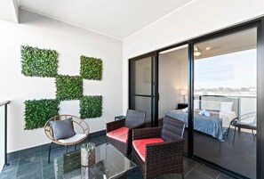 Een balkon met rieten meubels, een glazen tafel en wanddecoratie met planten.