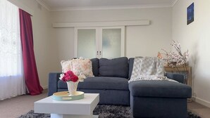 A living room with a sofa, a coffee table with a vase of flowers, a grey rug, and a window with curtains.