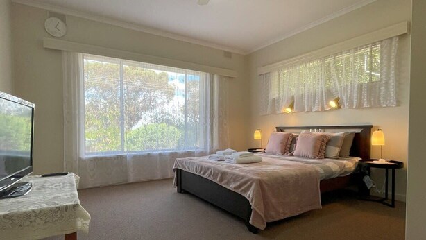 A bedroom with a bed, bedside lamps, a TV on a table, and large windows.