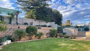 A backyard with a grassy lawn, a stone wall, and various plants.