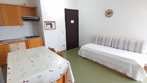 Quarto pequeno e aconchegante com cozinha compacta, mesa de jantar, sofá e uma porta.