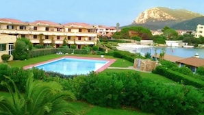 Um hotel com piscina, vegetação exuberante e uma montanha ao fundo.
