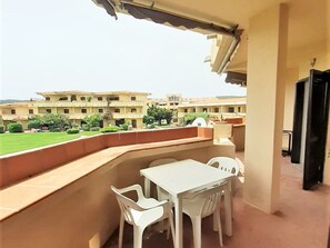 A balcony with a white table and chairs, overlooking a courtyard with buildings and greenery. - Belvilla by OYO Apartment in Golfo Aranci (Golfo Aranci)
