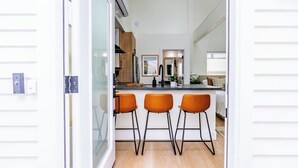 A modern kitchen with a central island, three orange bar stools, and a view into the adjacent living area. - Swanky Studio in Vibrant Hillcrest (San Diego)