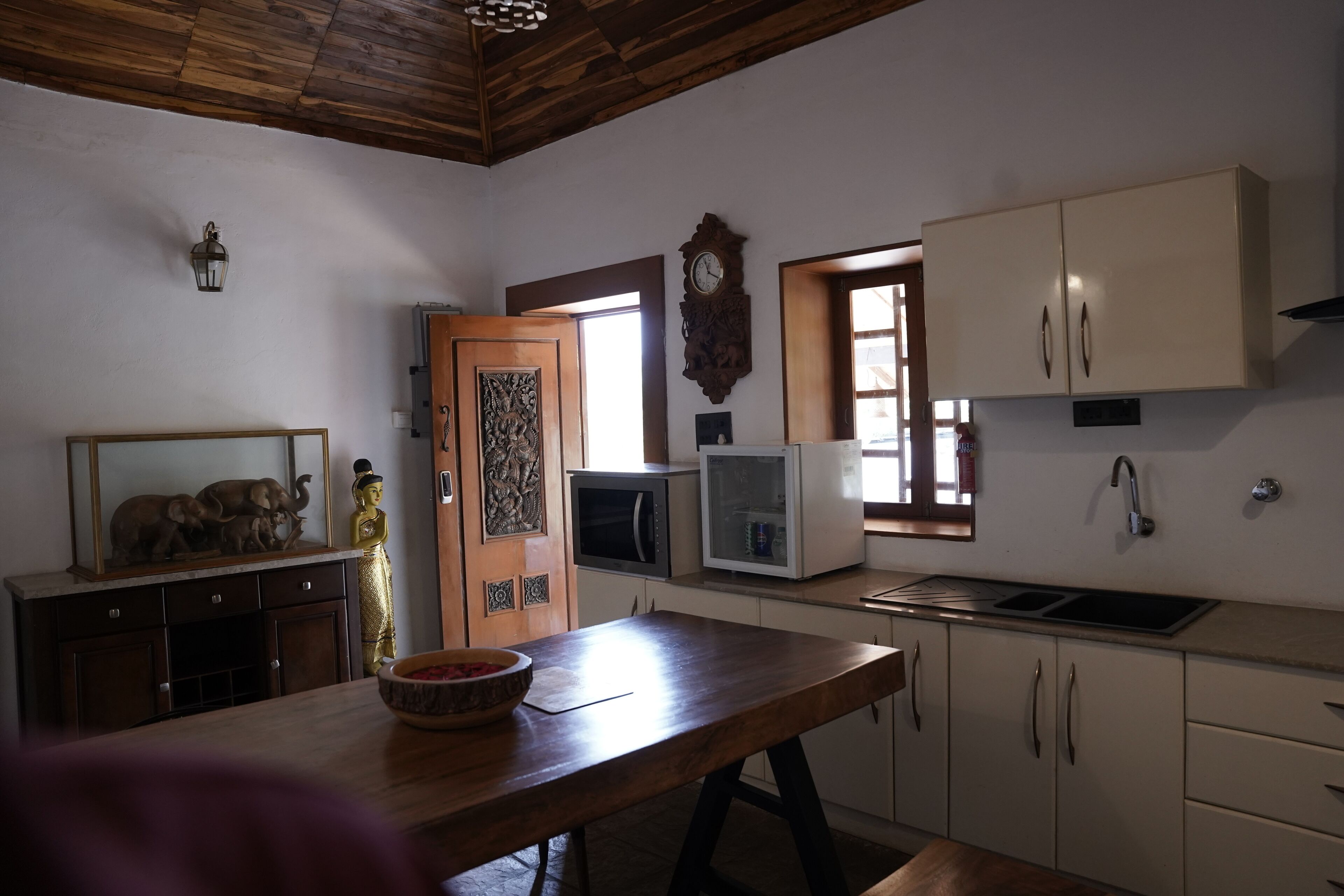 Una cocina con armarios de madera, microondas, pileta y una estatua decorativa de Buda.