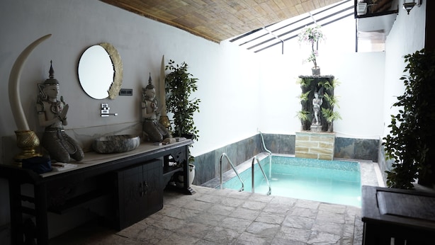 Un espace de bien-être doté d’une piscine en pierre, d’un plafond en bois et de statues décoratives.