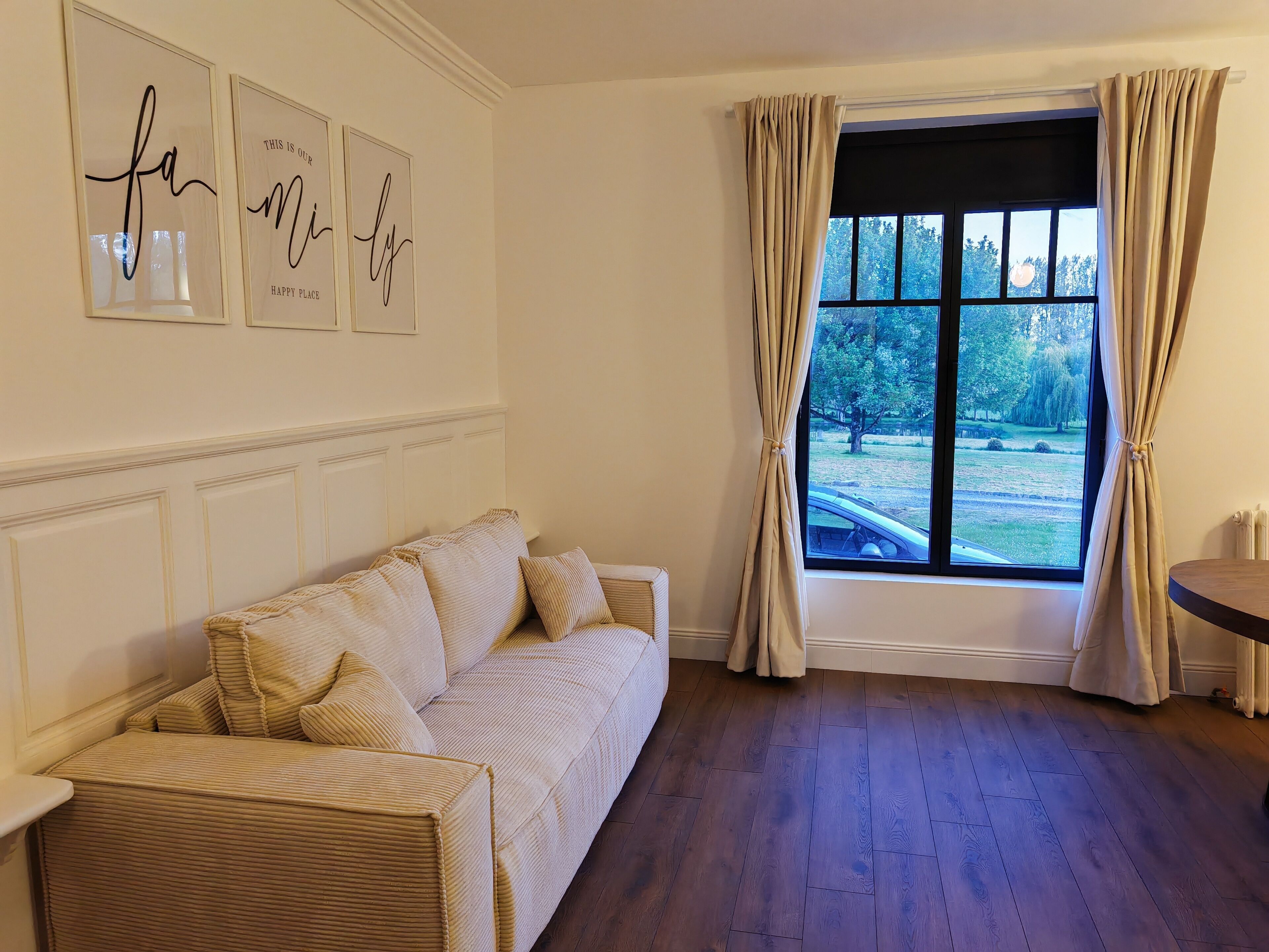 Una habitación con un sofá color beige, una ventana con cortinas y tres letreros enmarcados en la pared.