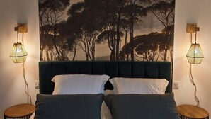Un dormitorio con una cama grande, cabecera verde oscuro y un mural de árboles. Hay dos mesitas de noche con lámparas.