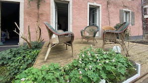 Ein pinkfarbenes Gebäude mit drei offenen Türen, Korbstühlen und einem Gartenbereich mit Grünpflanzen.