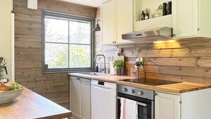 Een keuken met houten kastjes, een roestvrijstalen afzuigkap, een vaatwasser en een raam met uitzicht op bomen.