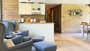 Een moderne woonkamer met grijze banken en poefjes, een houten vloer en een keuken met houten wanden en witte kasten.