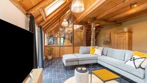 A modern living room with a sectional sofa, a round coffee table, and a TV. The room features wooden beams and a sloped ceiling with skylights. - Holiday Home in Reest Valley Near Forest & Pond (IJhorst)