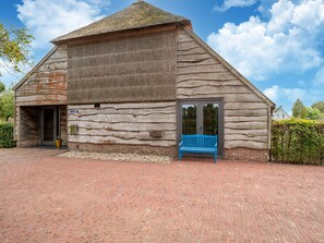 A rustic barn-style building with a large wooden door and a blue bench outside. - Holiday Home in Reest Valley Near Forest & Pond (IJhorst)
