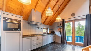 A modern kitchen with white cabinets, a stove, and a large window overlooking a blue deck. - Holiday Home in Reest Valley Near Forest & Pond (IJhorst)