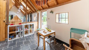 A cozy room with a wooden ceiling, a small table with chairs, a bookshelf, and a window with curtains. - Holiday Home in Reest Valley Near Forest & Pond (IJhorst)