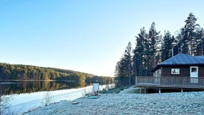 A cabin with a deck overlooking a lake, surrounded by trees. - 6 Person Holiday Home in Hornnes (Evje)