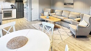 A modern kitchen with a built-in oven and refrigerator, a dining area with a round table and chairs, and a living room with a sofa and a coffee table. - 6 Person Holiday Home in Hornnes (Evje)