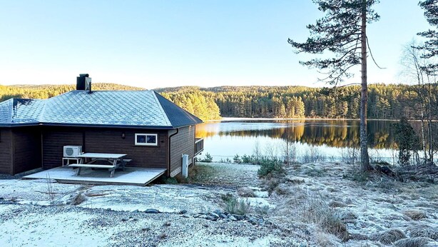 A cabin with a metal roof, a small porch, and a view of a lake surrounded by forest. - 6 Person Holiday Home in Hornnes (Evje)