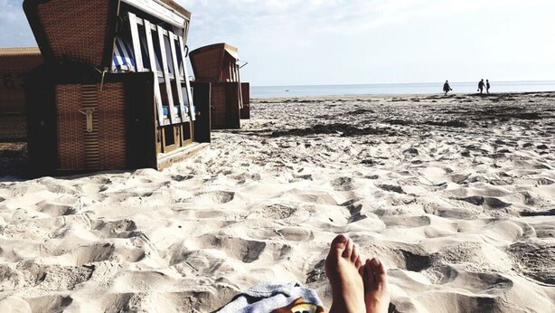 Una playa con una estructura de madera, posiblemente una cabaña, y arena con huellas.