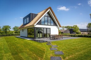 A modern house with a large glass window, a thatched roof, and a well-maintained lawn. - Villa in Texel Near Wadden Sea Lighthouse (De Cocksdorp)