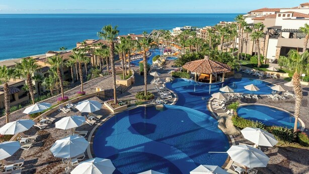 Een resort met meerdere zwembaden, palmbomen en uitzicht op de oceaan.