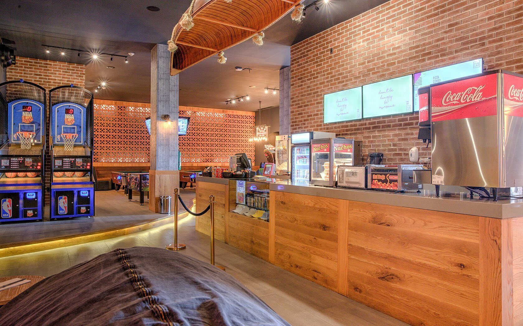 Een restaurant met sportthema, met basketbalspelletjes, een Coca-Cola koelkast en een balie met nachos.