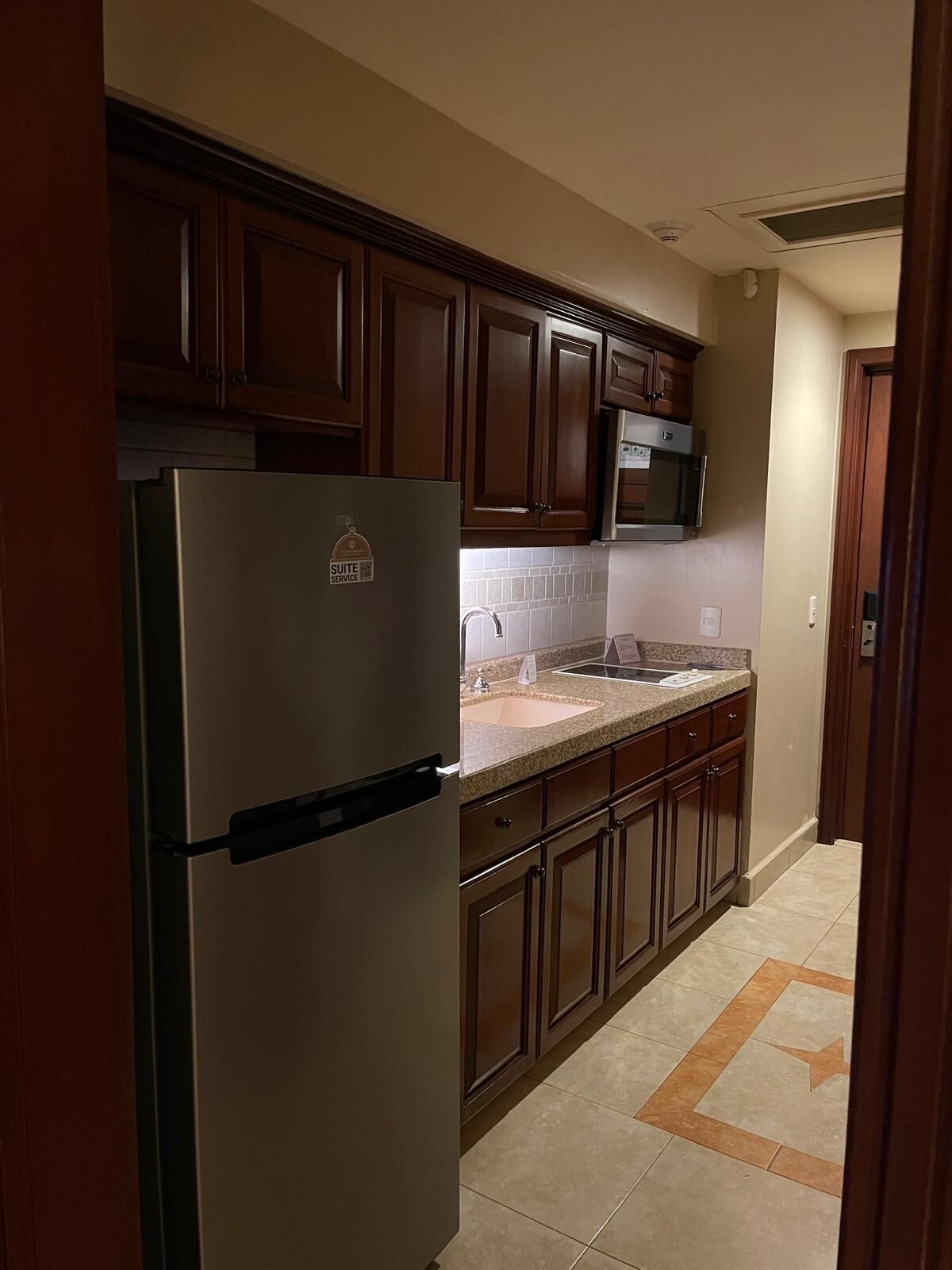 A kitchen with wooden cabinets, a stainless steel refrigerator, a microwave, and a granite countertop sink.