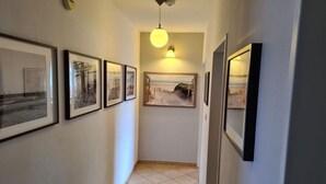 A hallway with framed artwork on the walls, a ceiling light, and a tiled floor.