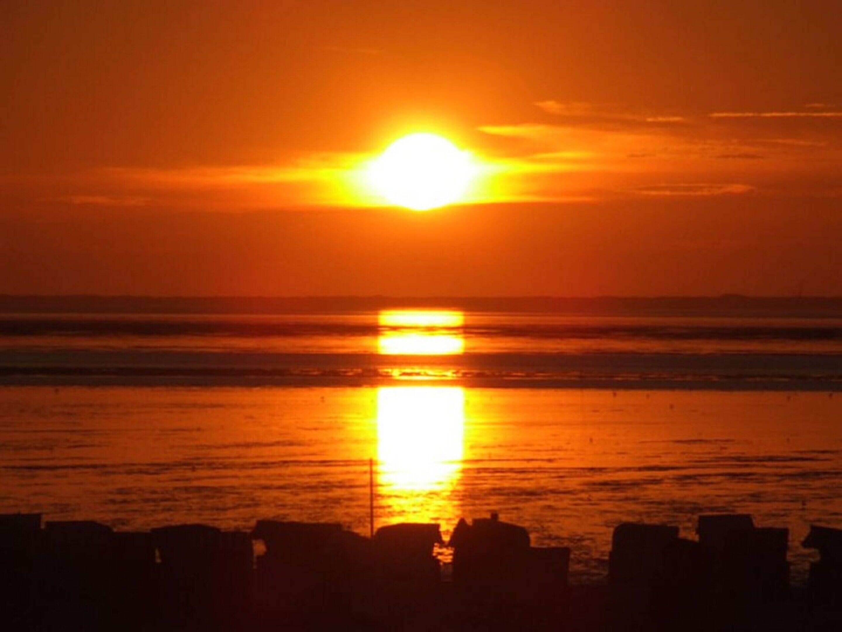 A sunset over a beach with silhouettes of beach chairs and a distant shoreline.