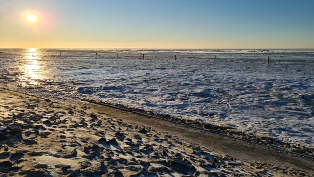 A beach with a clear sky and the sun setting or rising over the water.