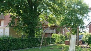 A residential garden with a swing set, a lawn, and a hedge.
