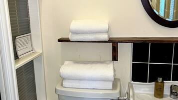 Een badkamer met toilet, wastafel, spiegel en een plank met een opgerolde handdoek.