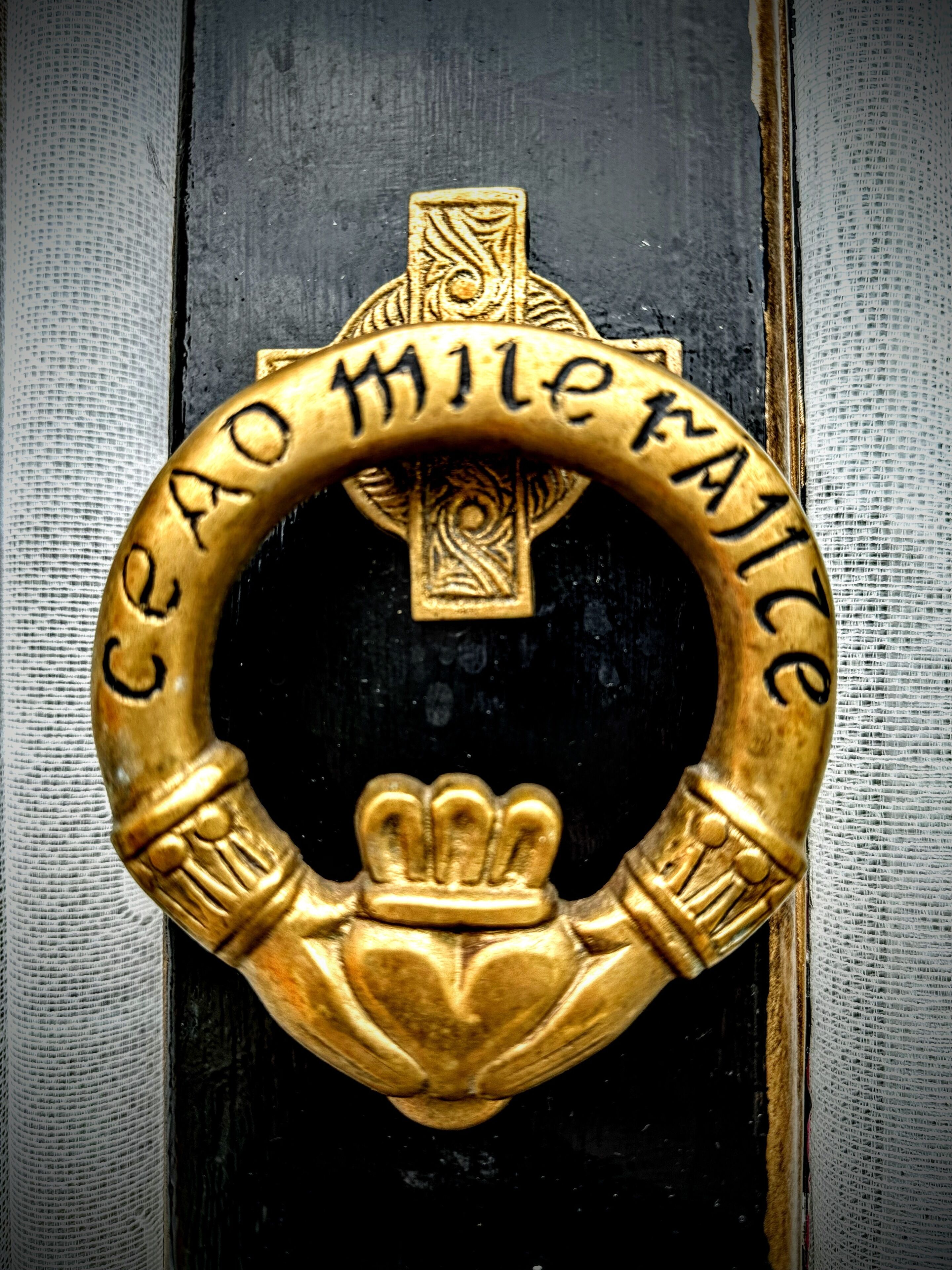 A golden door knocker with the inscription "Cao Milé Faicce".