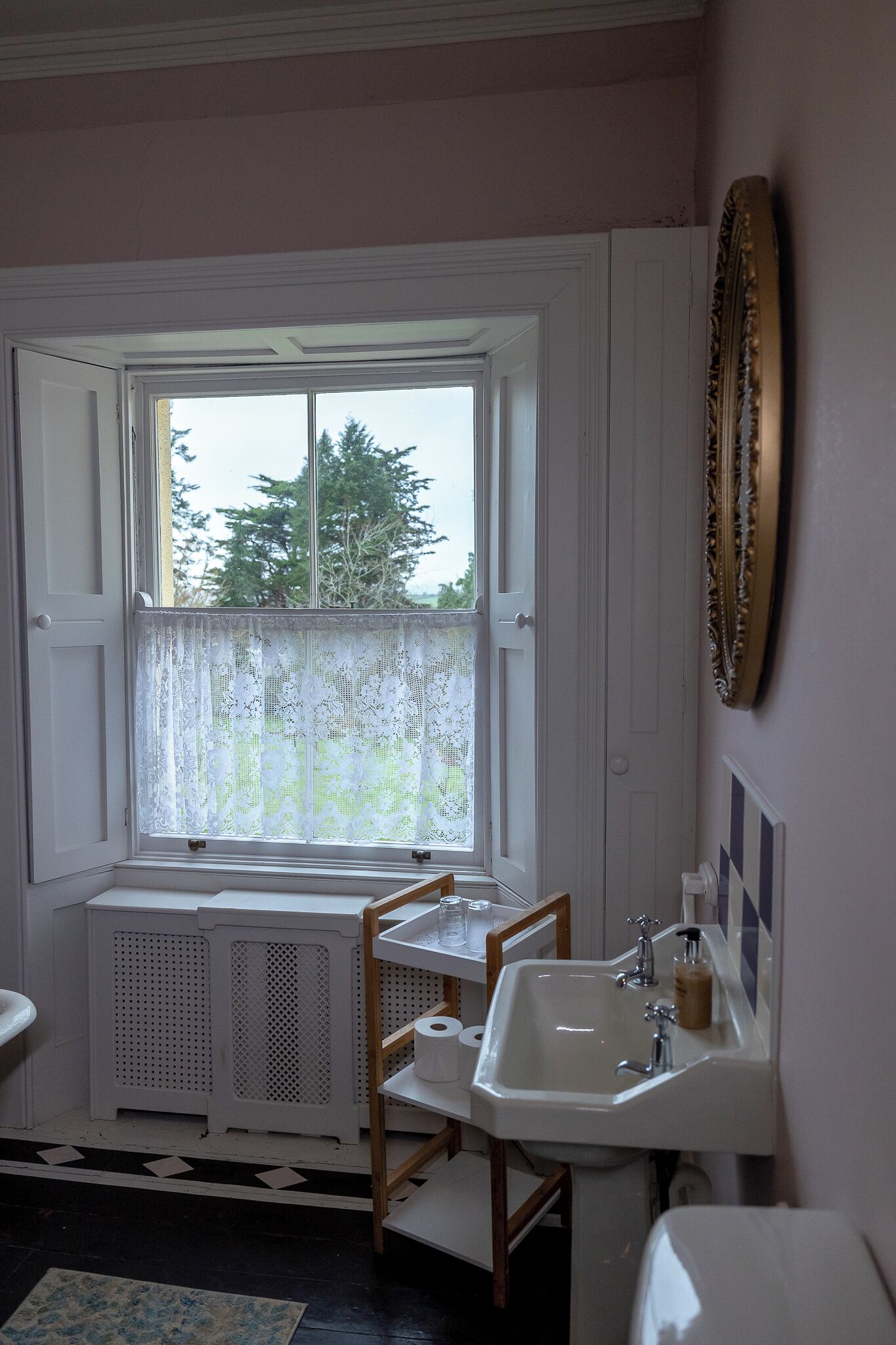 Une salle de bain avec une fenêtre, un lavabo, un miroir et un radiateur.