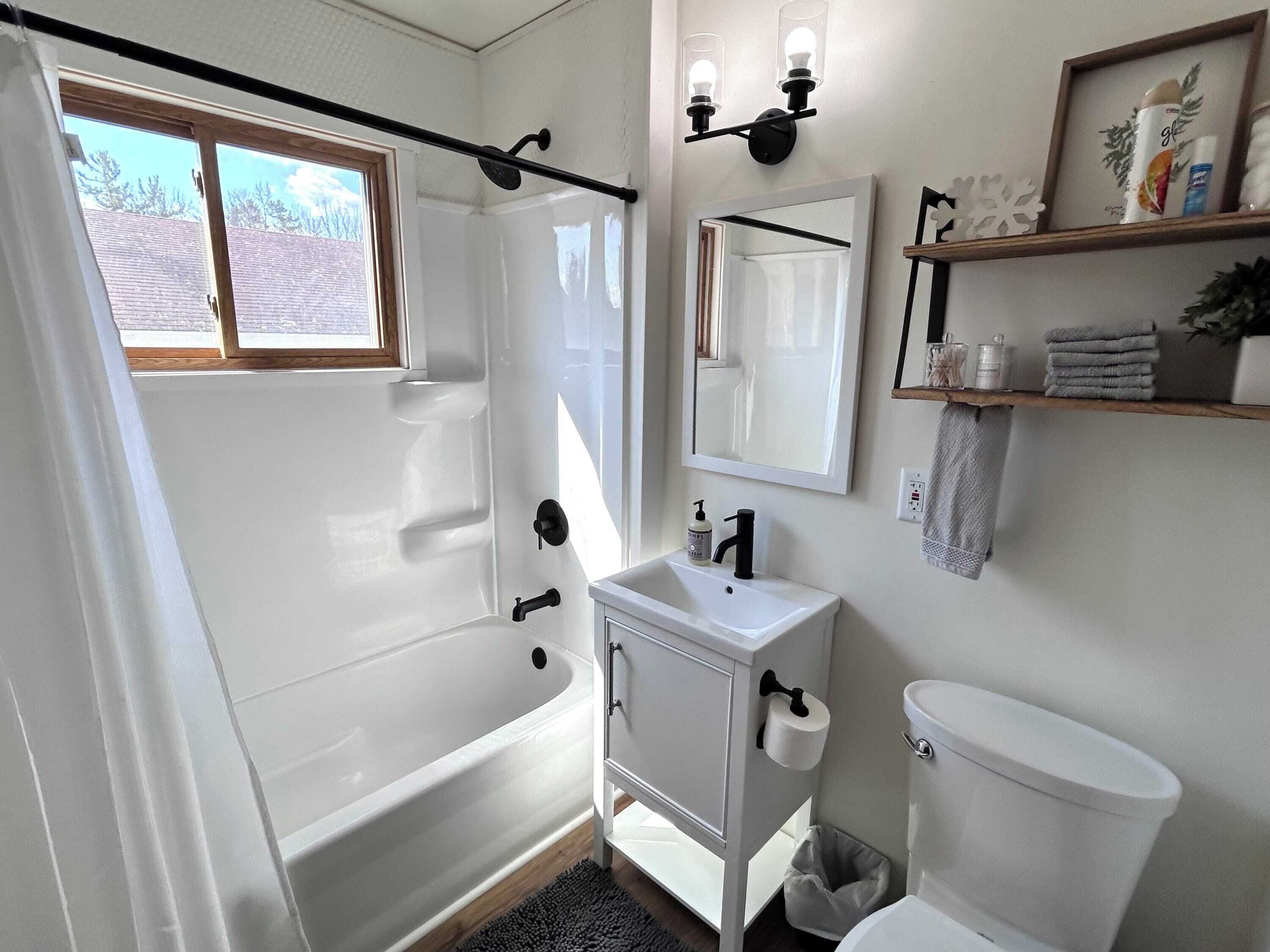 Un baño con bañera, lavabo, inodoro, cortina de ducha, ventana y espejo.