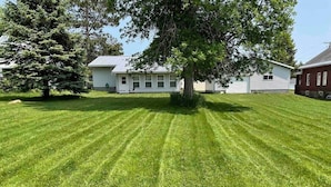 A well-maintained lawn with a large tree in the center, surrounded by a house with a white exterior and a red brick section.