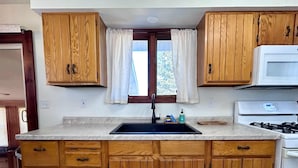 A kitchen with wooden cabinets, a sink, a stove, and a window with curtains.