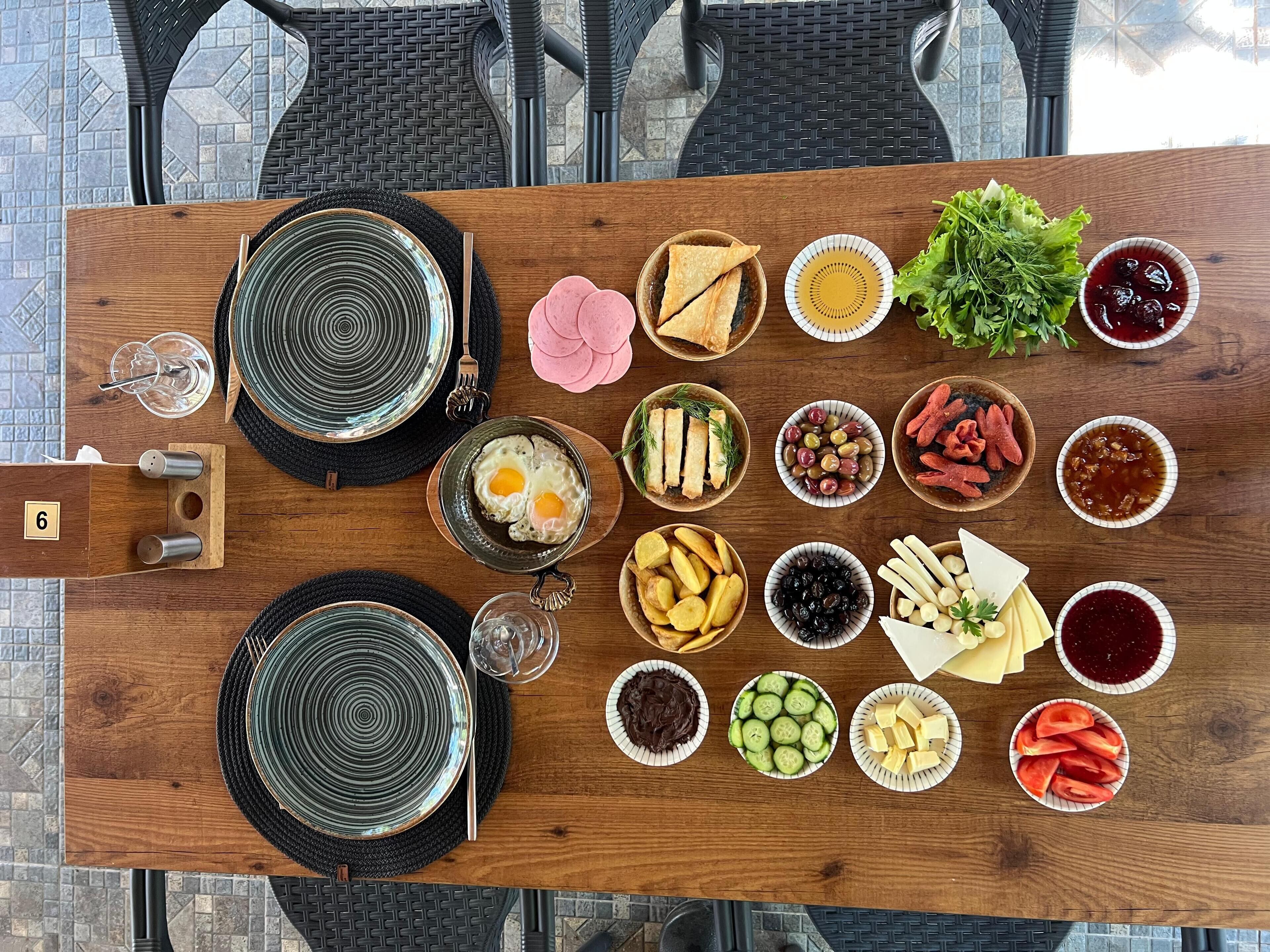A wooden table with various food items and condiments, surrounded by black chairs.