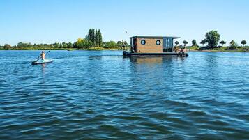 A houseboat with a small deck and a flag, floating on calm water.