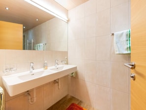 A modern bathroom with a white sink, two faucets, a mirror, and a towel rack.