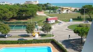 Vista de uma área costeira com piscina, uma estrada com carros e edifícios ao fundo.