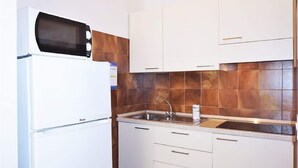 Cozinha compacta com armários brancos, micro-ondas embutido, pia de aço inoxidável e painel de azulejos.