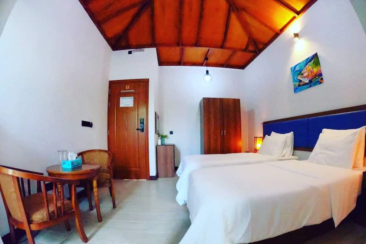 Habitación de hotel con dos camas, un armario de madera, un escritorio con sillas y un techo con vigas de madera.