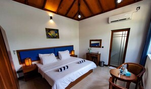 Ein Hotelzimmer mit Bett, Nachttischen, einem Sessel, einem Schreibtisch, einer Klimaanlage und einem Spiegel.