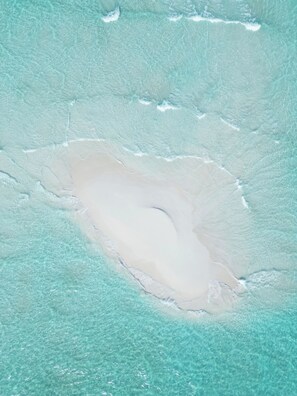 Ein Luftbild von einem Strand mit klarem türkisblauem Wasser und einer weiten Sandfläche.